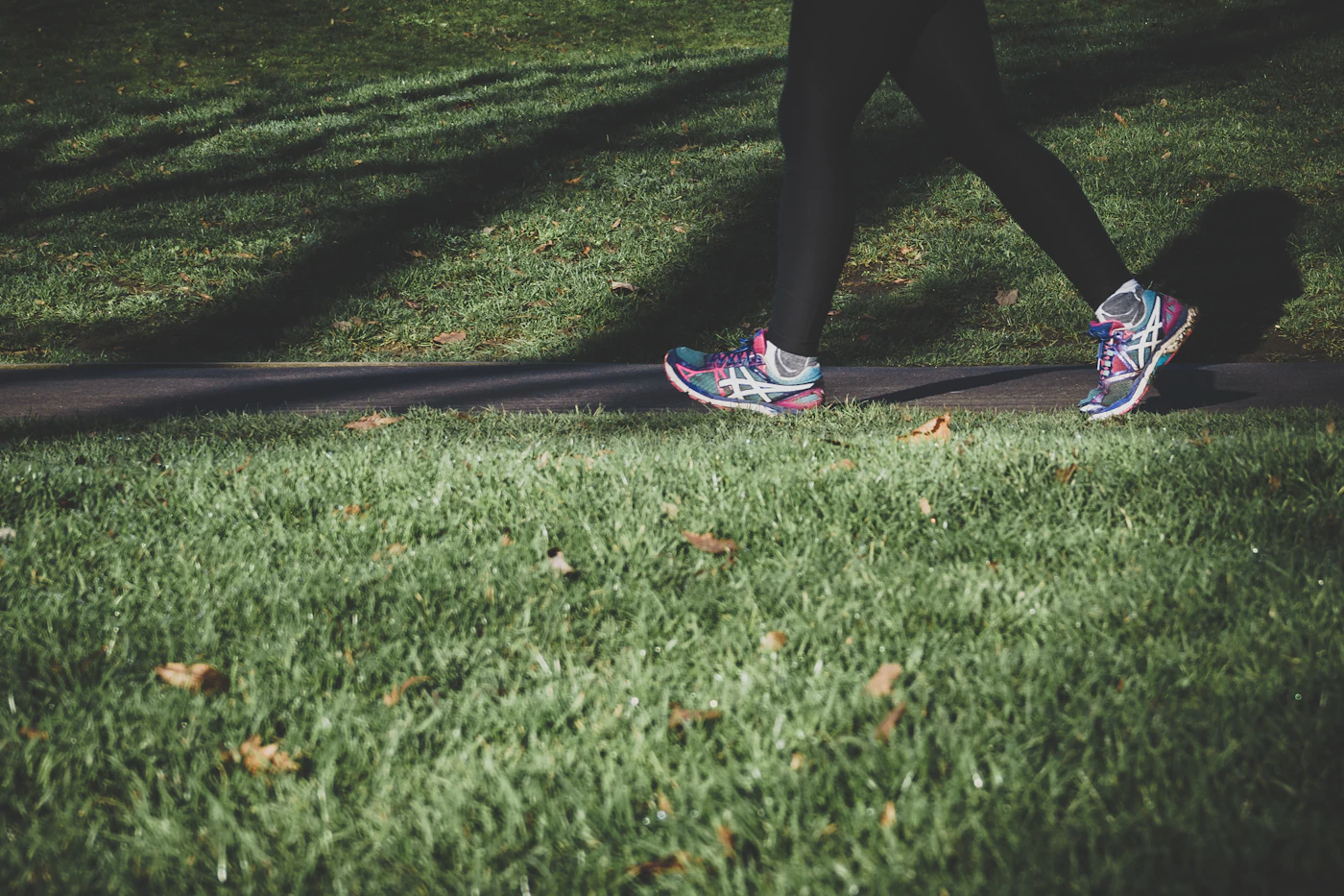 Person walking in sneakers on a paved path between grass